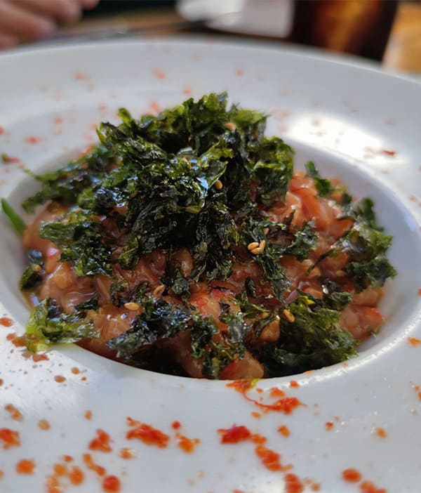 Imagen con Tartar de Salmón marinado en Ponzu sobre base de espagueti de pepino, rocotto rayado y algas fritas deshidratadas en aceite de sésamo